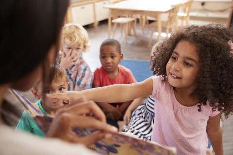 Girl pointing at something in book while other kids look on