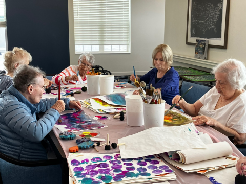 Five people painting papers around a table