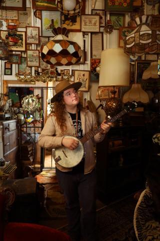 Photo of the presenter, Ben Traverse, standing in an antiques shop with his banjo.