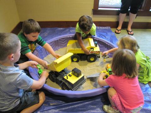 Five kids playing in a sandbox with construction vehicles