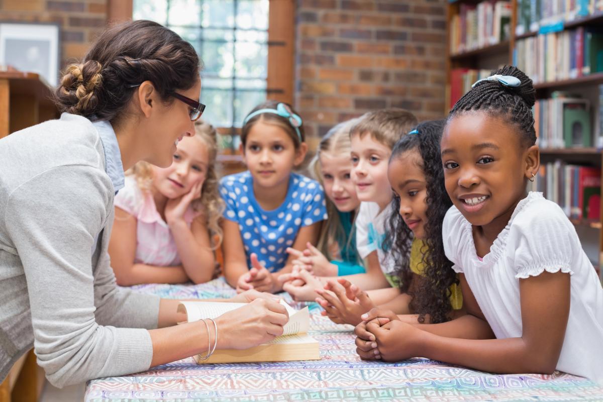 Kids huddled together looking at a book with a woman