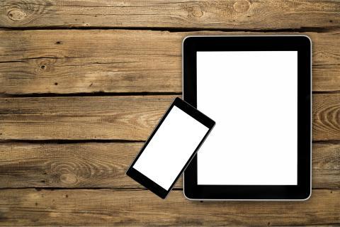 a tablet and a smartphone sitting on a wooden surface.